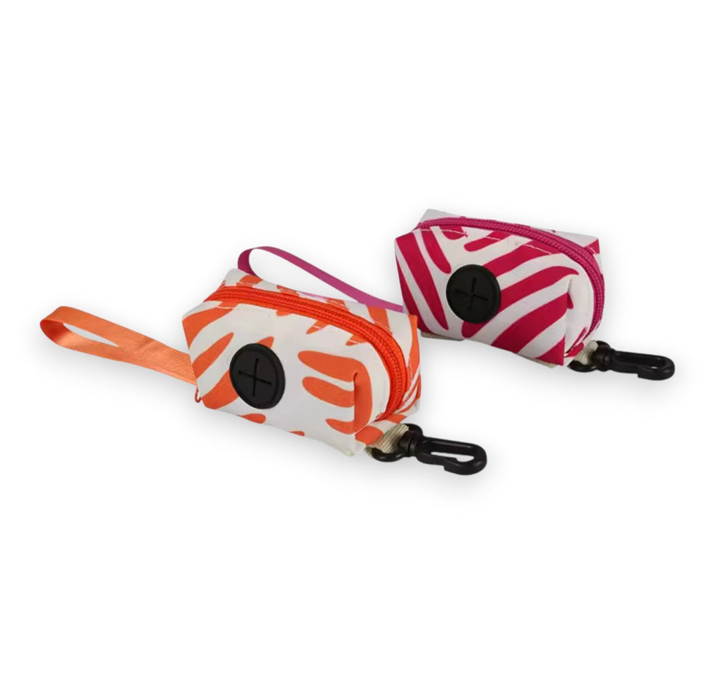 Set of two patterned fabric pet waste bag dispensers; one orange, one pink. Both have black carabiner clips.